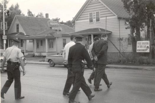  Dickinson Police escort the burglars to police cars. In the background is The Rock Shop, which was located near present-day U-Save Car Wash